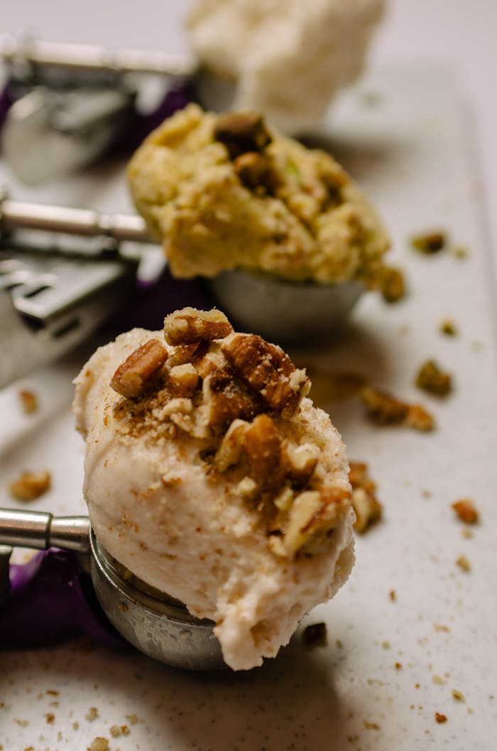 Close-up shot of ice cream scoops garnished with nuts on a textured surface.