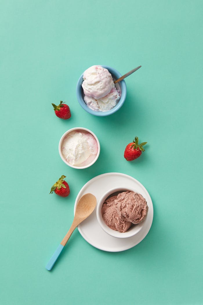 Flat lay of ice cream scoops with strawberries on a pastel blue background. Perfect for food and dessert themes.
